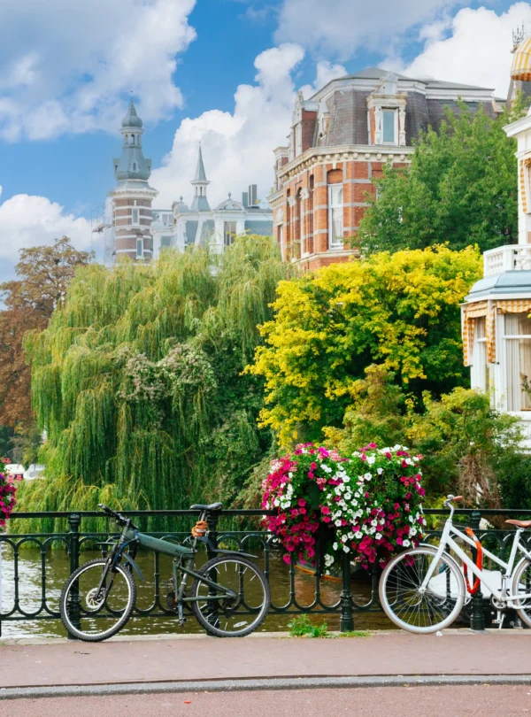 Charming Amsterdam canal scene with bicycles lined along a flower-adorned bridge, framed by historic architecture and lush greenery — a quintessential stop on our IzzyTrip Netherlands tours.