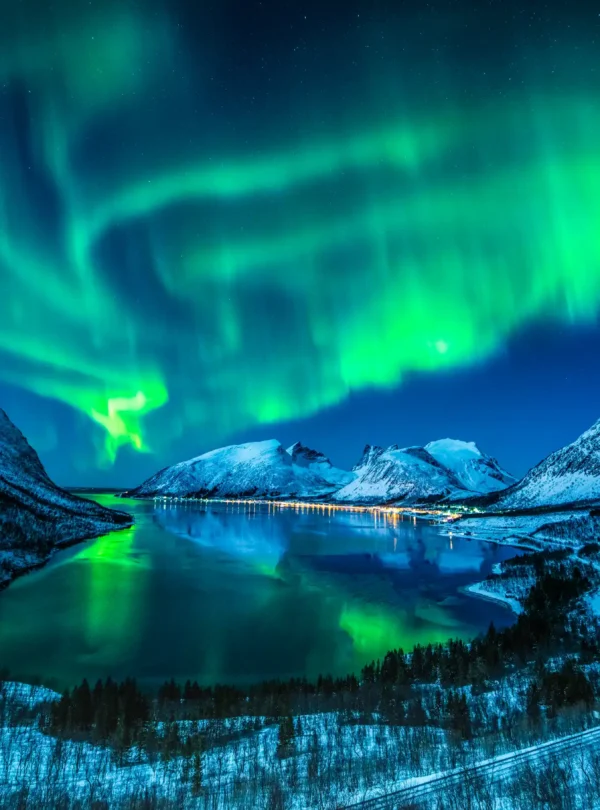Dazzling Northern Lights dancing over snow-covered fjords in Tromsø, Norway, their vivid green glow reflecting on the icy waters — an unforgettable Arctic adventure with IzzyTrip.
