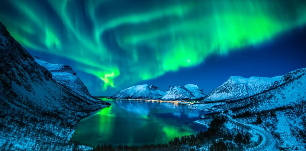 Dazzling Northern Lights dancing over snow-covered fjords in Tromsø, Norway, their vivid green glow reflecting on the icy waters — an unforgettable Arctic adventure with IzzyTrip.