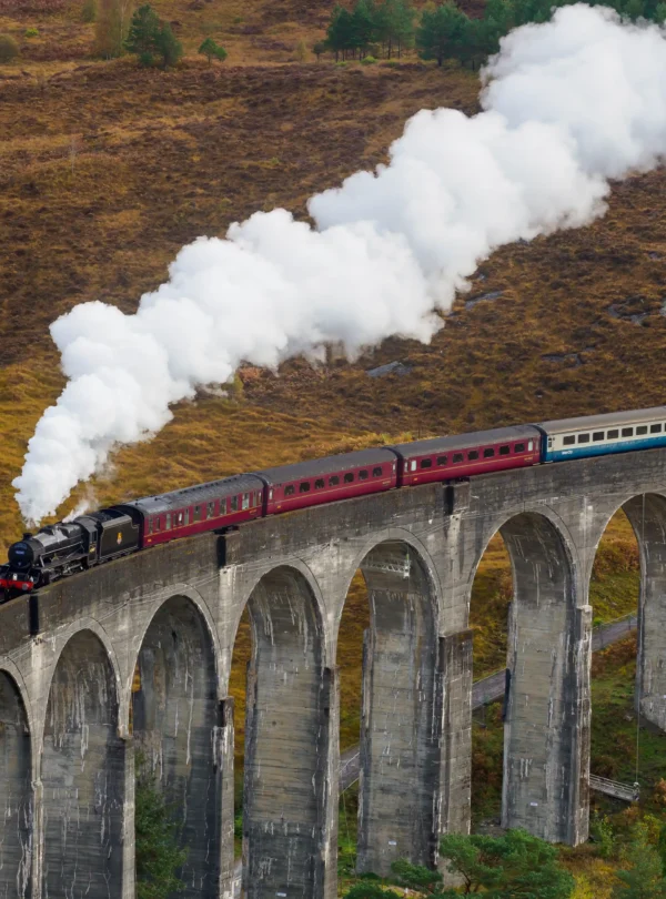 Steam train crossing the Glenfinnan Viaduct in the Scottish Highlands, surrounded by rugged landscapes — an iconic scene featured on IzzyTrip’s Scotland tours.